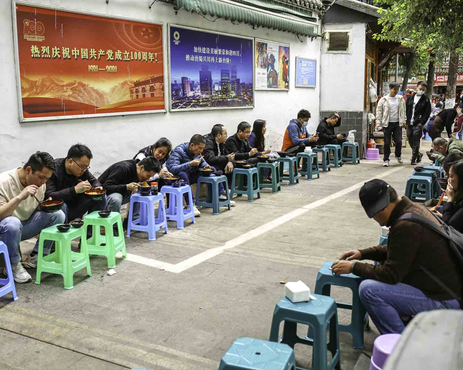Locals sitting on the sidewalk with their noodles
